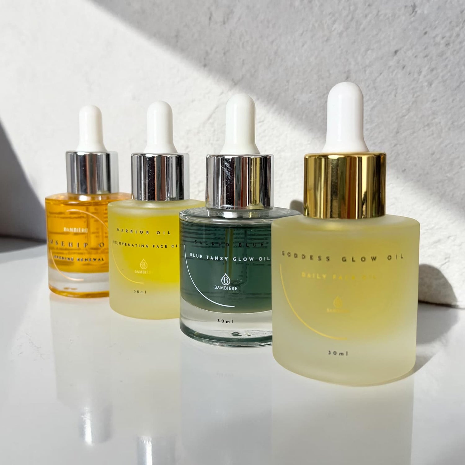Four skincare oil dropper bottles on a white surface with a light gray background