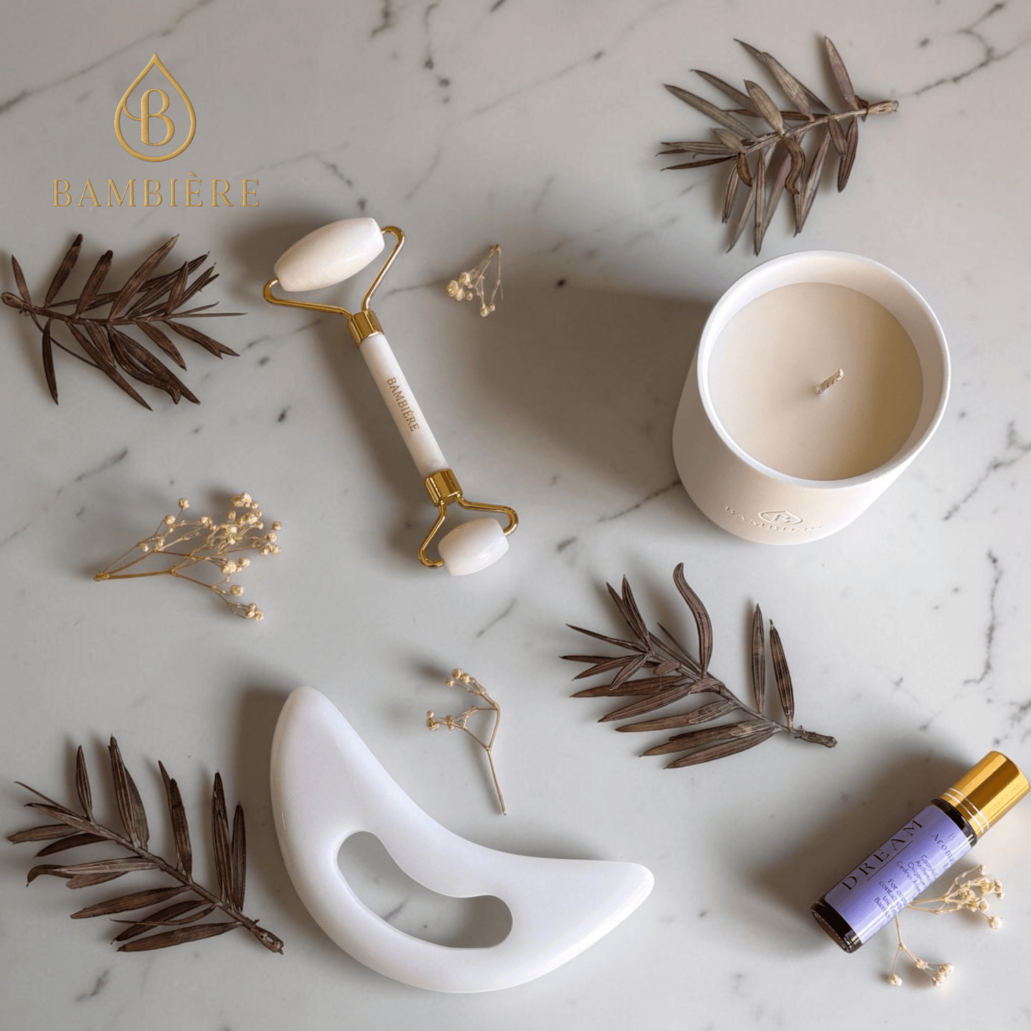 Skincare tools and candle on a marble surface with dried leaves and flowers.